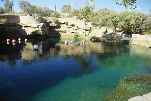 A serene swimming hole surrounded by rocky cliffs and trees, featuring colorful buoys floating on clear water.