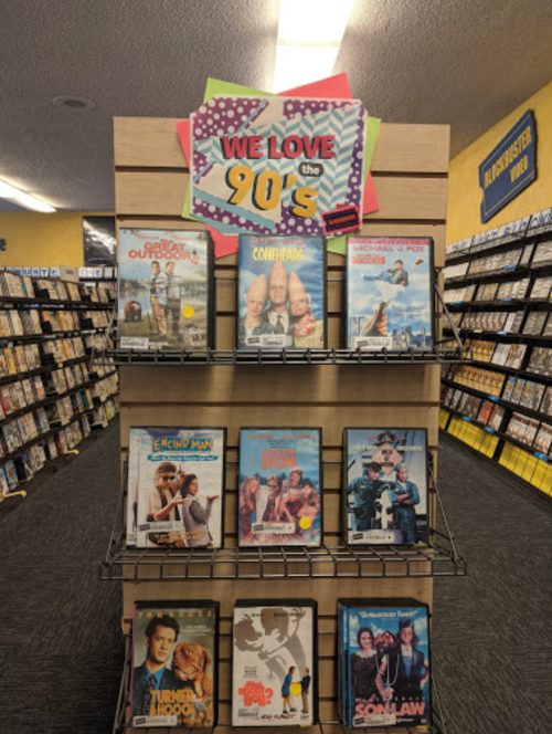 A display rack featuring 90s movies with a sign that says "WE LOVE the 90s" in a video rental store.
