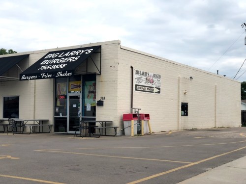 Exterior of Big Larry's Burgers, featuring a drive-thru, outdoor seating, and a sign advertising burgers, fries, and shakes.