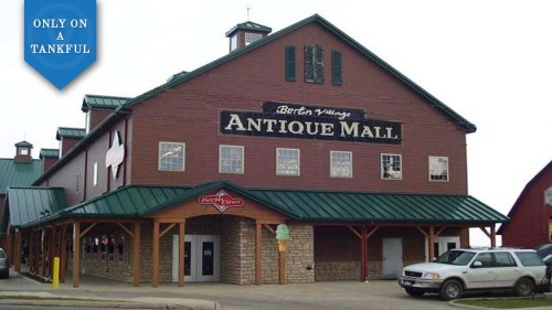 A large, rustic building with a green roof and sign reading "Antique Mall," featuring a stone base and multiple windows.