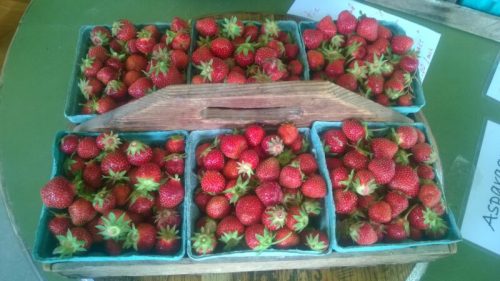 A wooden basket filled with fresh strawberries in small containers on a table.