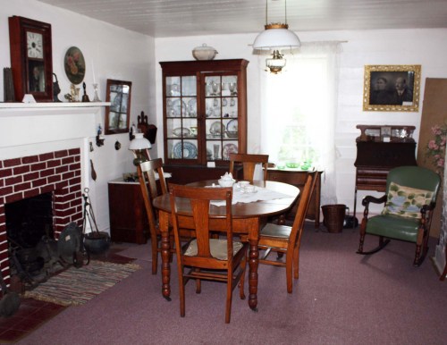 Cozy dining room with a wooden table, chairs, a china cabinet, and a fireplace, featuring vintage decor and soft lighting.