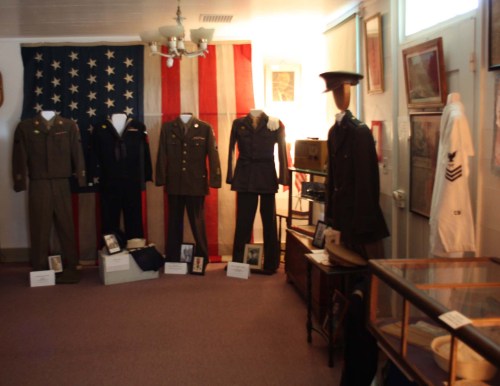 A military museum display featuring uniforms, a large American flag, and historical photographs.