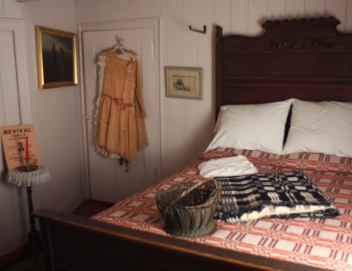 A cozy bedroom featuring a wooden bed, vintage dress on a hanger, and decorative items on a side table.