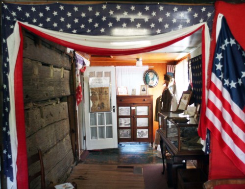 Interior of a historic room decorated with American flags, featuring wooden walls and vintage furniture.