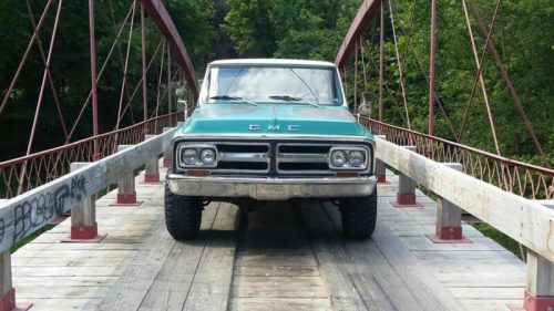 A vintage GMC truck parked on a wooden bridge surrounded by greenery.