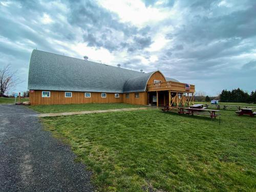 A large wooden barn with a curved roof, surrounded by green grass and picnic tables, under a cloudy sky.