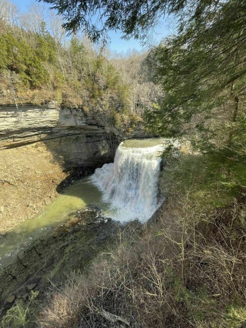 A serene waterfall cascading over rocky cliffs, surrounded by trees and a peaceful natural landscape.