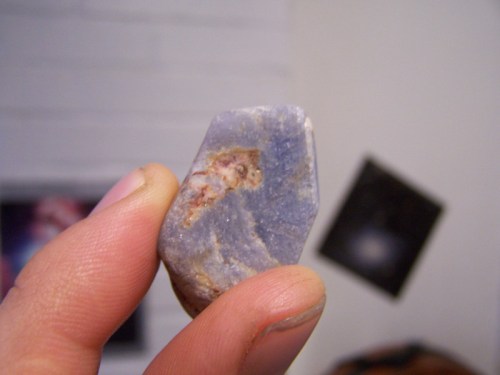 A person holding a small, irregularly shaped blue stone with some reddish-brown markings against a blurred background.