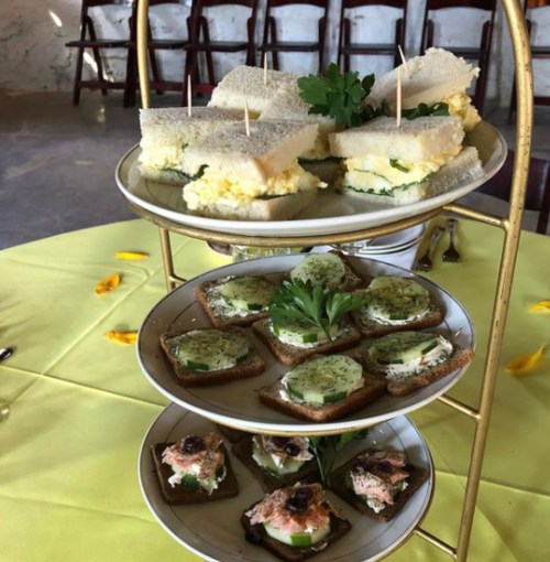 A tiered serving platter with sandwiches and assorted canapés, set on a yellow tablecloth.