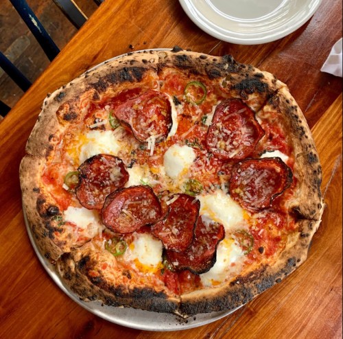 A freshly baked pizza topped with pepperoni, jalapeños, and melted cheese on a wooden table.