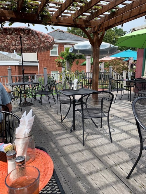 Outdoor dining area with empty black metal tables and chairs, shaded by umbrellas, on a wooden deck.
