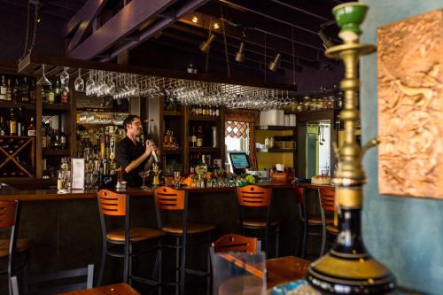 A bartender prepares drinks at a stylish bar with shelves of liquor and hanging glassware in a cozy setting.