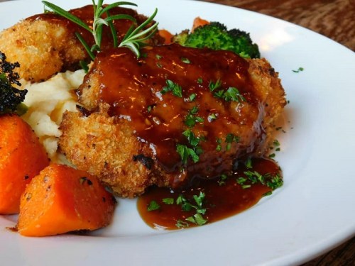 A plate of crispy fried chicken with gravy, served alongside mashed potatoes, broccoli, and roasted carrots.