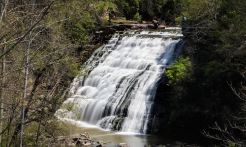 A cascading waterfall surrounded by lush greenery and rocky terrain, with a person standing nearby.