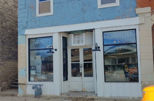 A blue storefront with large windows displaying "TURNERS" and a sign that says "We Are Open" on the door.