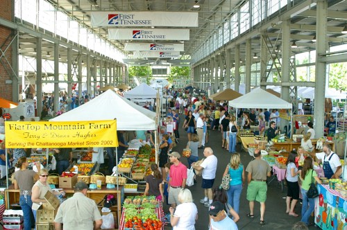 A bustling farmers market with vendors, tents, and crowds of people shopping for fresh produce and goods.
