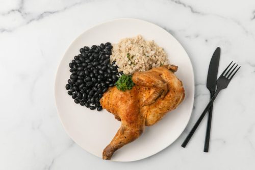 A plate with roasted chicken, black beans, and rice, garnished with parsley, on a marble surface.