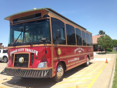 A red trolley bus with "Dodge City Trolley" written on the side, parked in a lot on a sunny day.