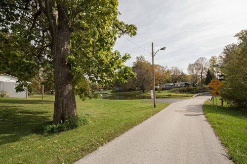 A peaceful road lined with trees, leading to a pond, with a warning sign for cyclists ahead.