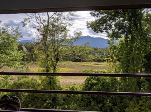 View from a balcony overlooking a lush landscape with trees and mountains under a partly cloudy sky.