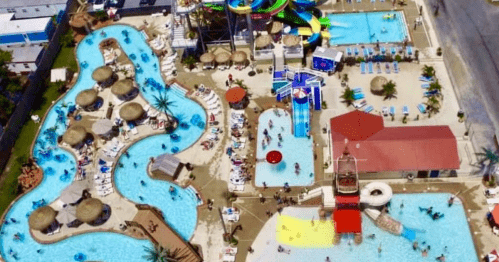 Aerial view of a vibrant water park featuring pools, slides, and lounging areas filled with people enjoying the sun.