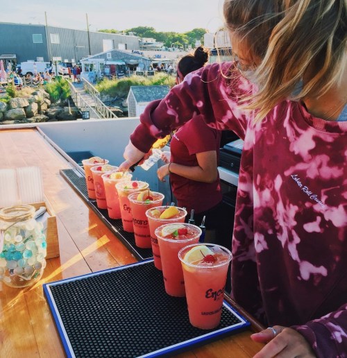 A bartender prepares colorful cocktails with fruit garnishes at a lively outdoor bar.