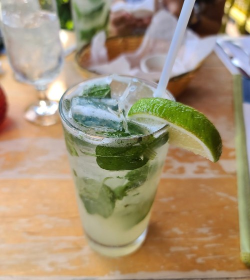 A refreshing mojito with mint leaves and a lime wedge, served in a clear glass with a straw on a wooden table.