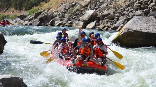 A group of people in orange life jackets paddling a red raft through whitewater rapids on a river.