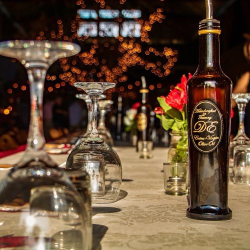 A beautifully set dining table with wine glasses, olive oil bottle, and flowers, illuminated by soft, warm lights.