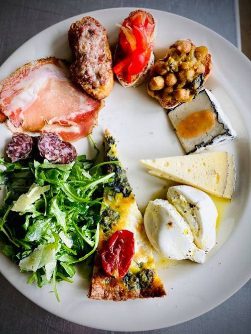 A plate featuring assorted meats, cheeses, a frittata, chickpeas, and a fresh arugula salad.