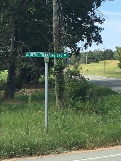 A green street sign reads "Devil Tramping Grd" next to a grassy area and a road.