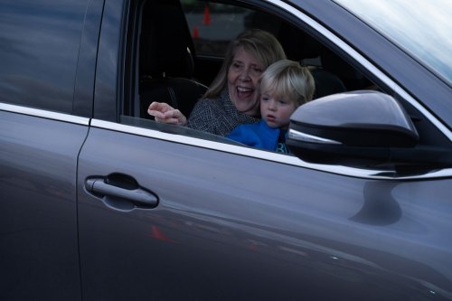 A woman and a young boy smile from the open window of a car, enjoying their time together.