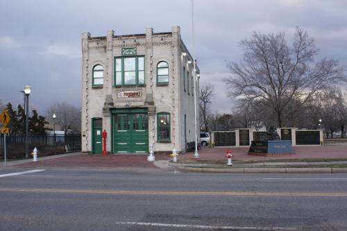 Historic building with green doors, surrounded by trees and a street, featuring a fire hydrant and plaques nearby.