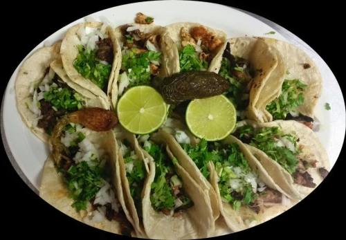 A platter of tacos filled with meat, onions, and cilantro, garnished with lime wedges and a roasted pepper.