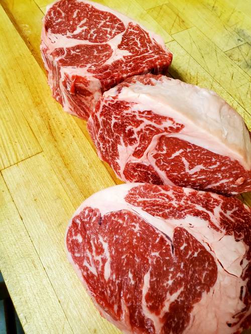 Three marbled cuts of beef resting on a wooden cutting board.