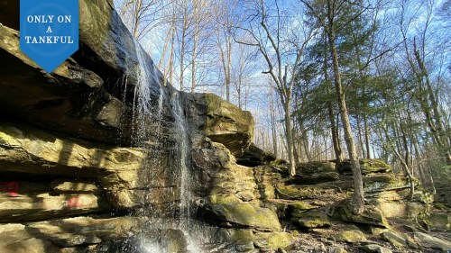 A serene waterfall cascading over rocky terrain, surrounded by trees under a clear blue sky.