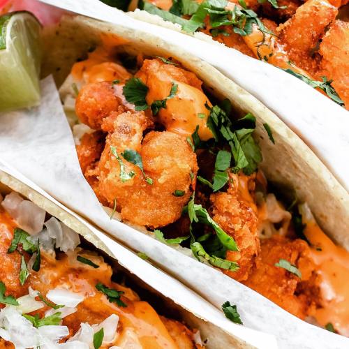 Three shrimp tacos topped with sauce and cilantro, served with lime wedges on the side.