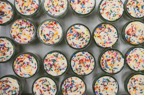 Aerial view of jars filled with creamy frosting topped with colorful sprinkles.