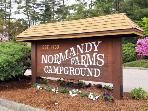 Sign for Normandy Farms Campground, established in 1759, surrounded by greenery and flowers.