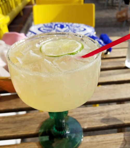 A refreshing margarita with a lime slice, served in a green glass on a wooden table.