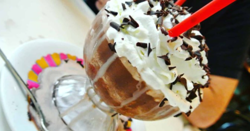 A delicious chocolate sundae topped with whipped cream, chocolate shavings, and two red straws in a glass dish.