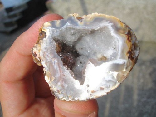 A hand holding a geode with a smooth, polished exterior and a crystalline interior.