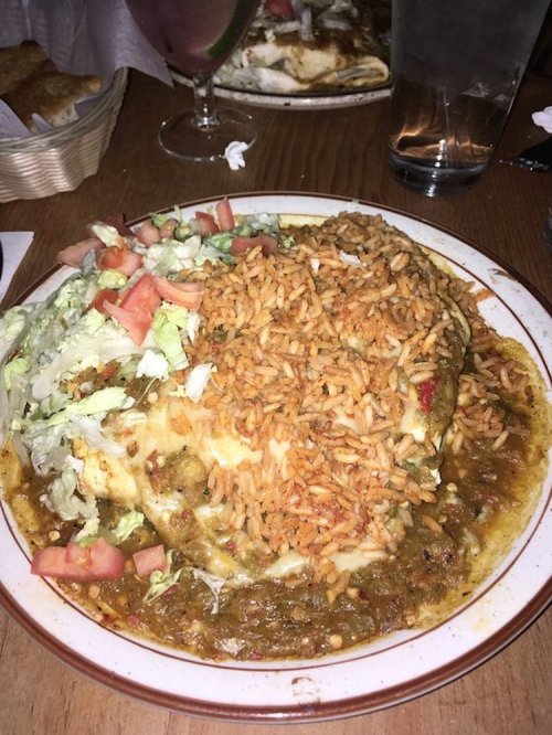 A plate of enchiladas topped with rice, lettuce, and tomatoes, served with a side of sauce.
