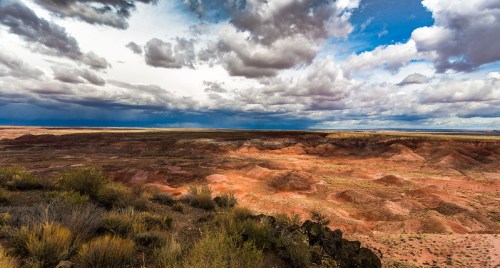 A panoramic view of a colorful desert landscape under a dramatic sky filled with clouds.