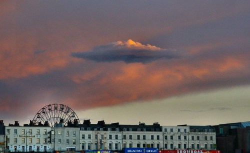 A sunset sky with colorful clouds above a seaside town, featuring a ferris wheel in the background.