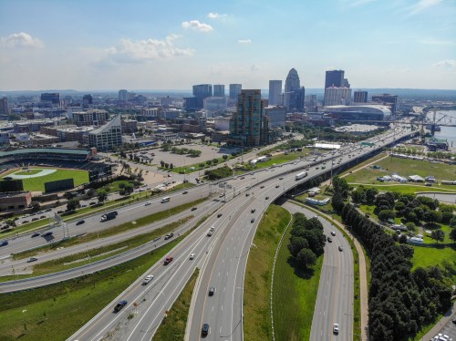 Aerial view of a city skyline with highways, green spaces, and buildings under a clear blue sky.