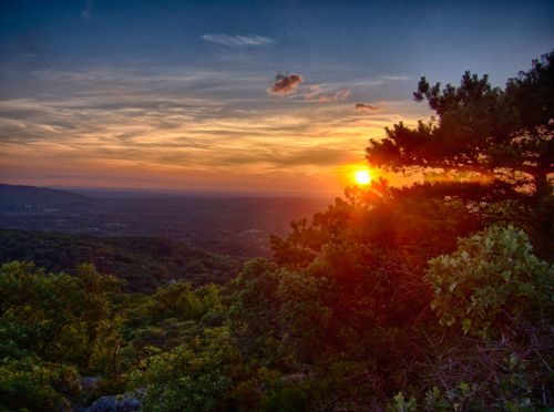 A vibrant sunset over a lush green landscape, with trees framing the view and colorful clouds in the sky.