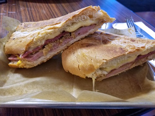A close-up of a sliced sandwich with layers of ham, cheese, and chicken on crusty bread, served on parchment paper.