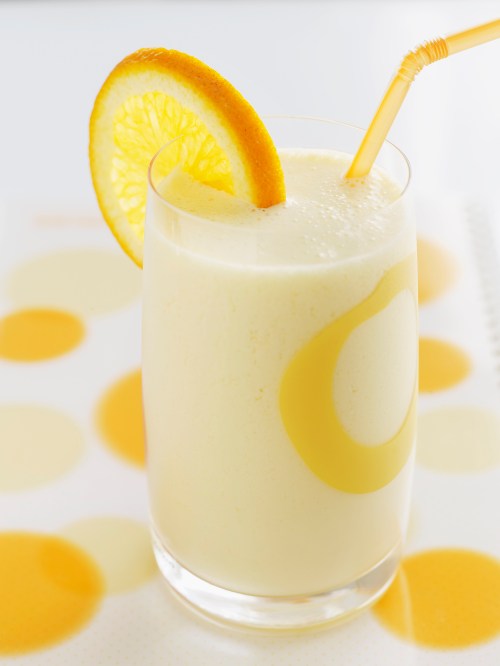 A refreshing yellow smoothie in a glass, garnished with a slice of orange and a straw, on a dotted yellow napkin.